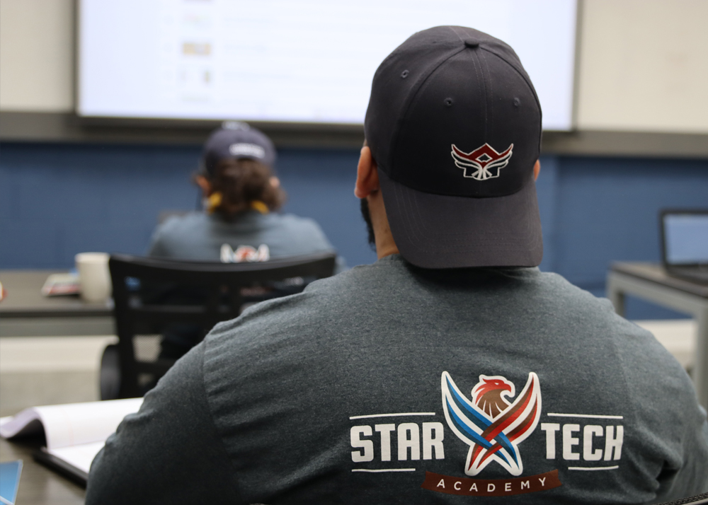 Man seated in class wearing a Star Tech Academy T-shirt with the logo on his back