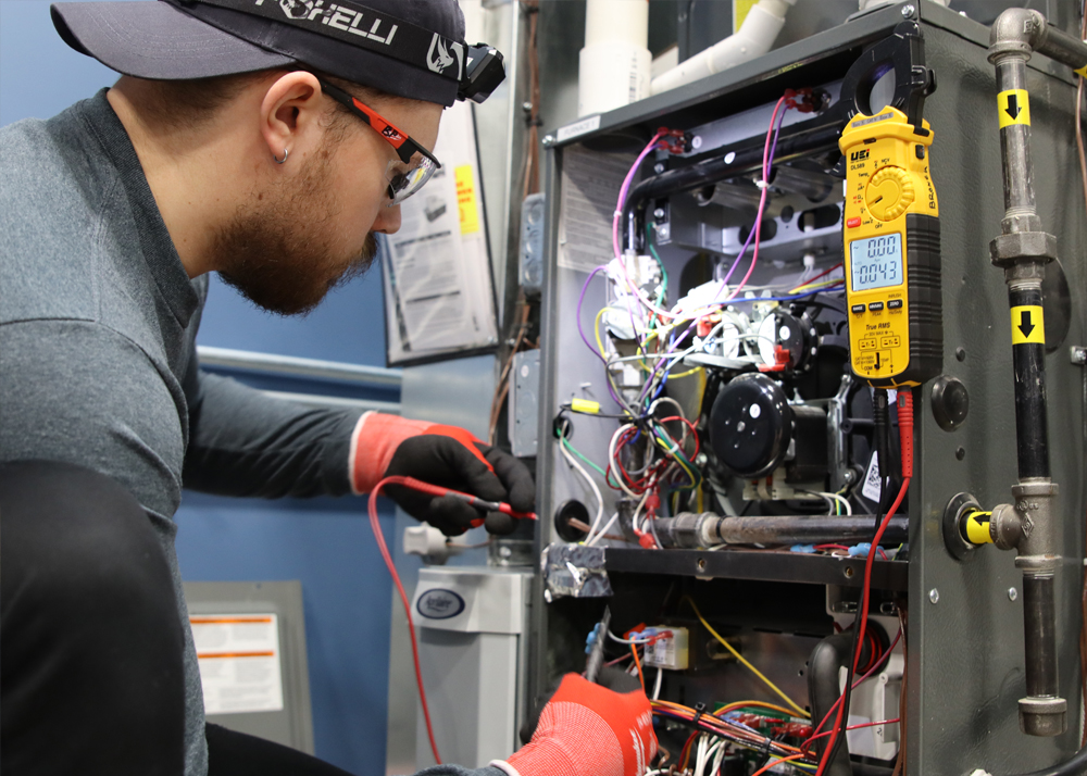 Professional technician working on the wiring of an opened equipment box with exposed wiring and a multimeter